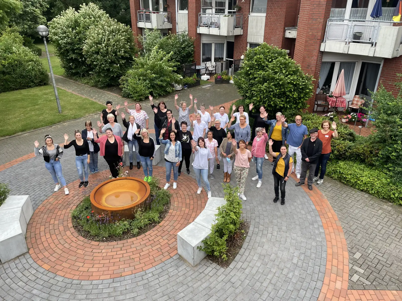 Das Team des Seniorenwohnheims St. Ludgerus steht im Innenhof und winkt in die Kamera